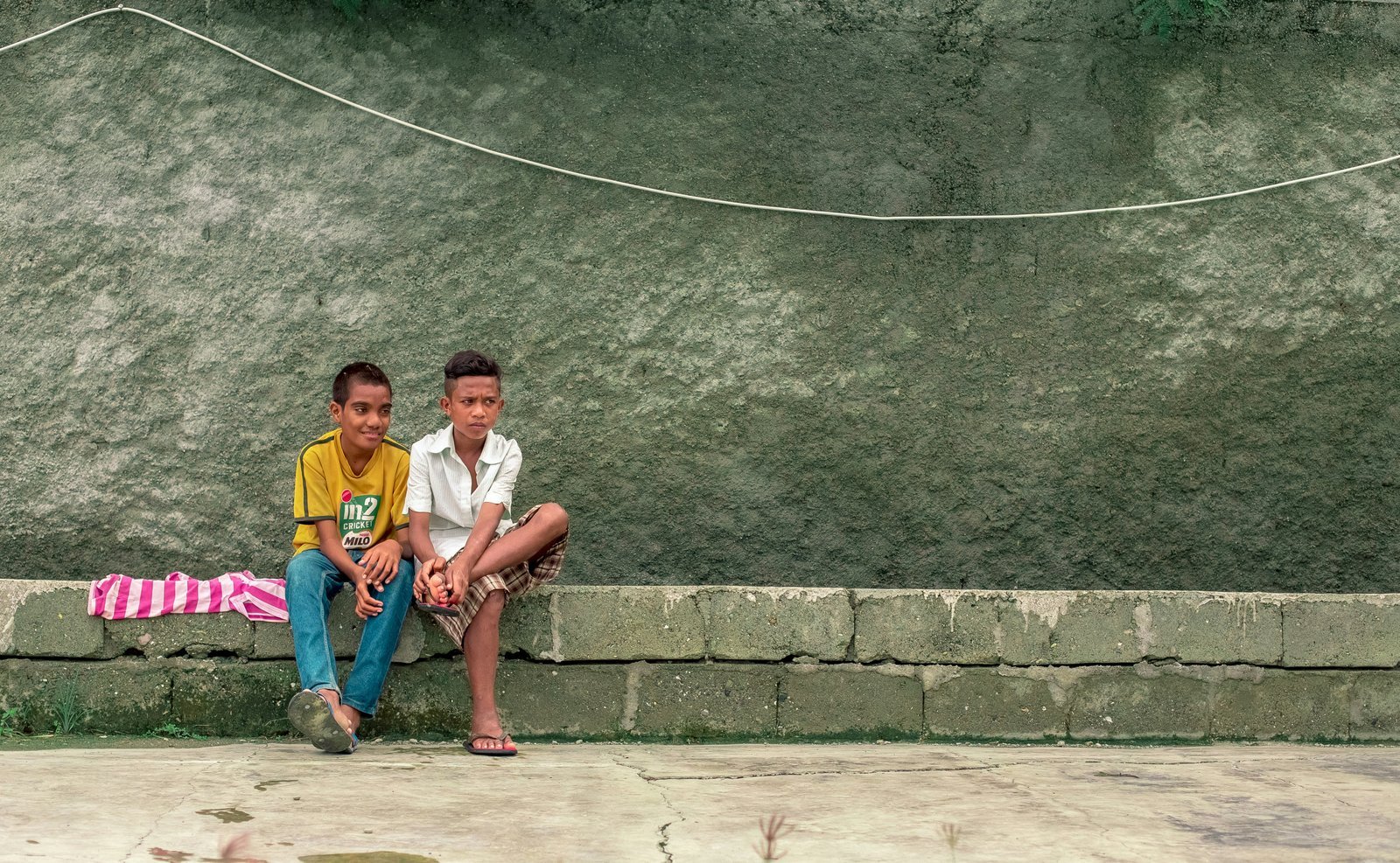 two boy sitting on gray pavement